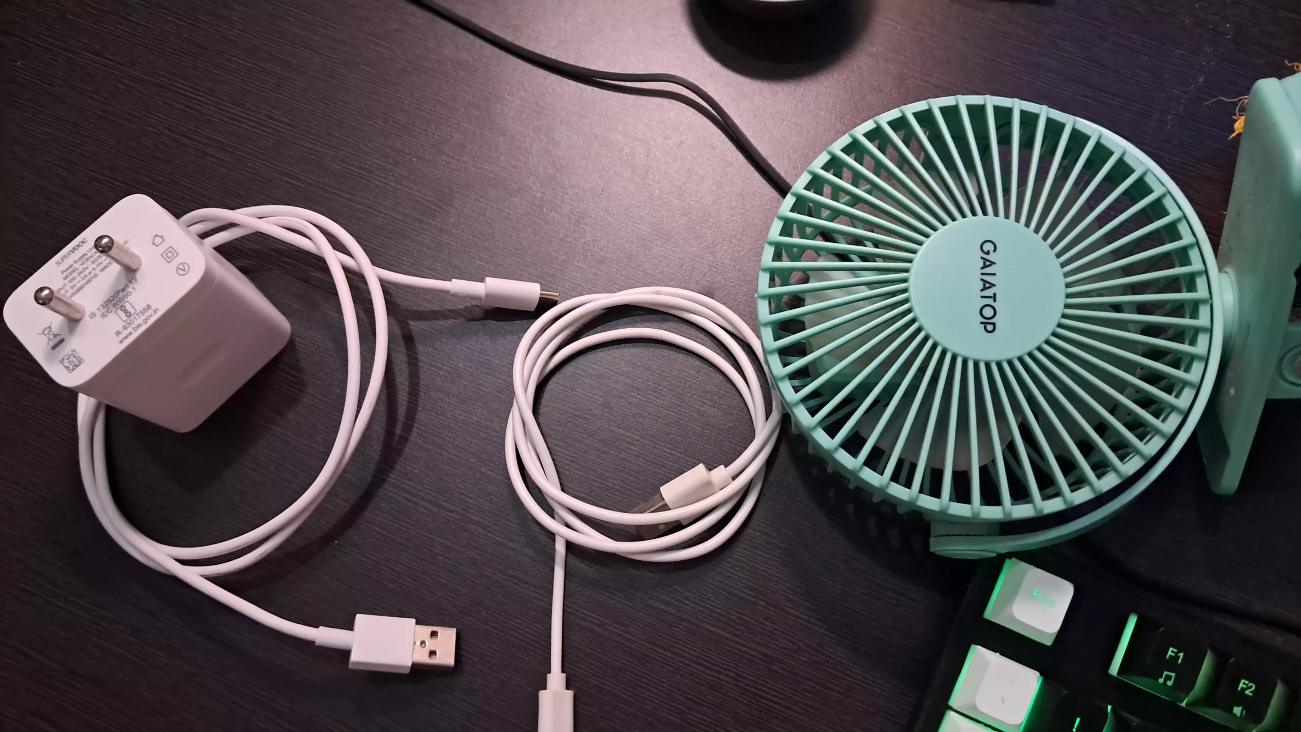 Two USB cables on the table with a charger and table top fan